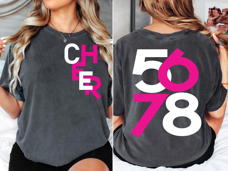 May include: A dark gray t-shirt with the word "CHEER" printed in white and pink on the front and the numbers "5678" printed in white and pink on the back.