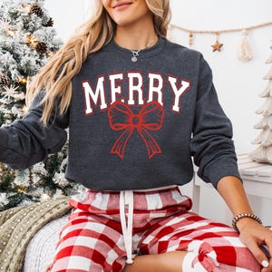 May include: A grey sweatshirt with the word "MERRY" in white letters and a red bow. The sweatshirt is being worn by a person wearing red and white checked trousers.