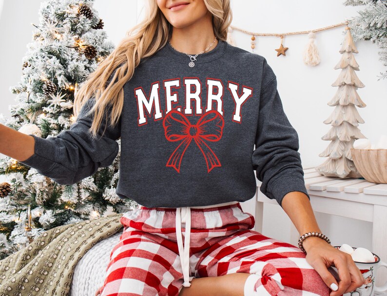 May include: A grey sweatshirt with the word "MERRY" in white letters and a red bow. The sweatshirt is being worn by a person wearing red and white checked trousers.