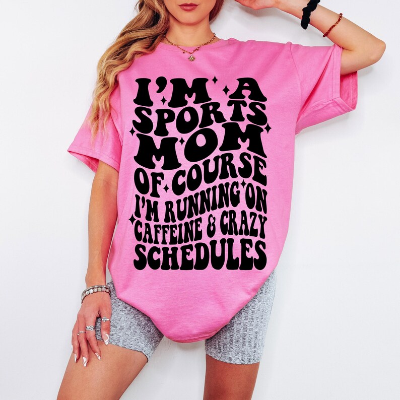 Pode incluir: Camiseta rosa com texto preto que diz "Eu sou uma m&atilde;e esportiva, claro que corro com cafe&iacute;na e hor&aacute;rios loucos".
