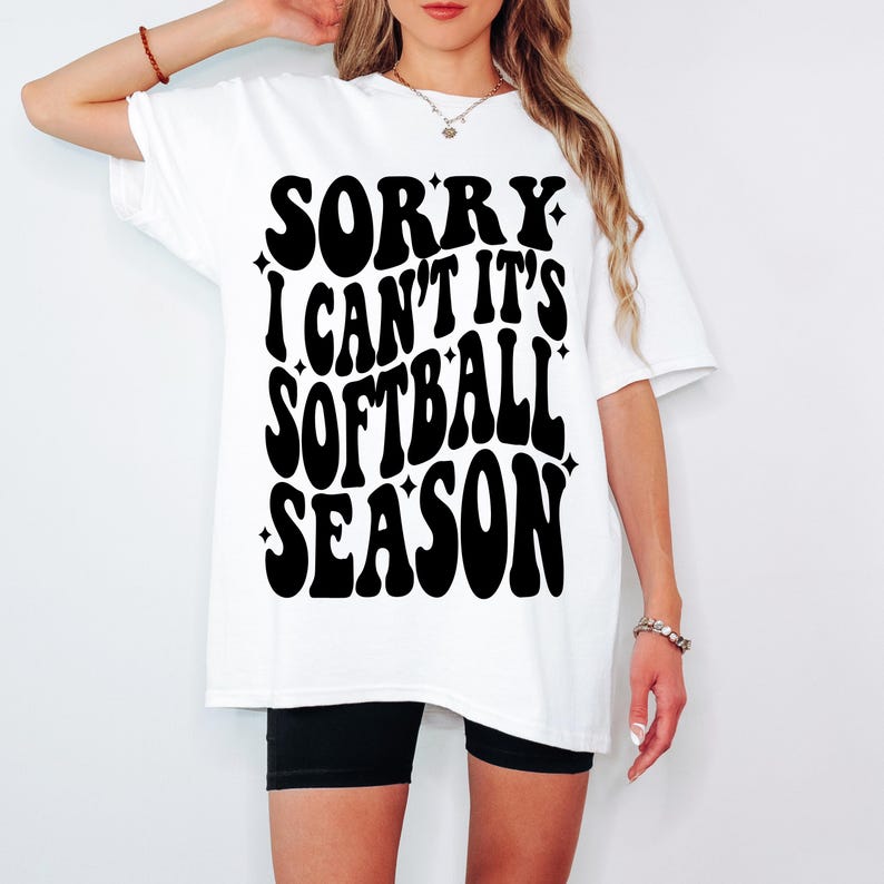 May include: White t-shirt with black text that reads "Sorry I can't it's softball season" in a retro font.