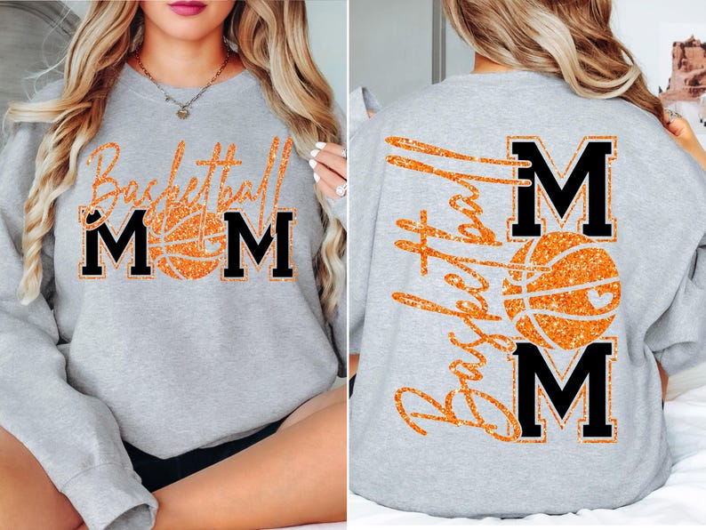 May include: A light gray sweatshirt with the words "Basketball Mom" in orange glitter lettering and a basketball graphic. The letters "MOM" are in black block letters. The back of the sweatshirt also features the words "Basketball Mom".
