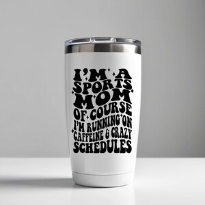 Pode incluir: Um copo t&eacute;rmico de a&ccedil;o inoxid&aacute;vel branco com um gr&aacute;fico preto que diz "Eu sou uma m&atilde;e esportiva, claro que eu corro na cafe&iacute;na e em hor&aacute;rios loucos".