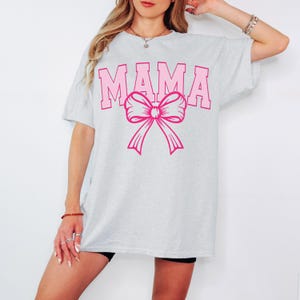 May include: A gray t-shirt with the word "MAMA" printed in pink letters with a pink bow underneath.