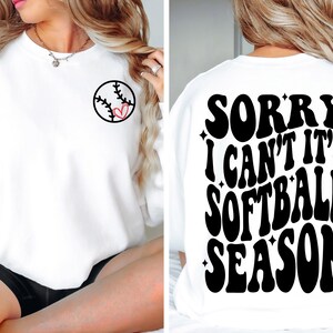 May include: White sweatshirt with a softball graphic on the front and the text "SORRY I CAN'T IT'S SOFTBALL SEASON" on the back.
