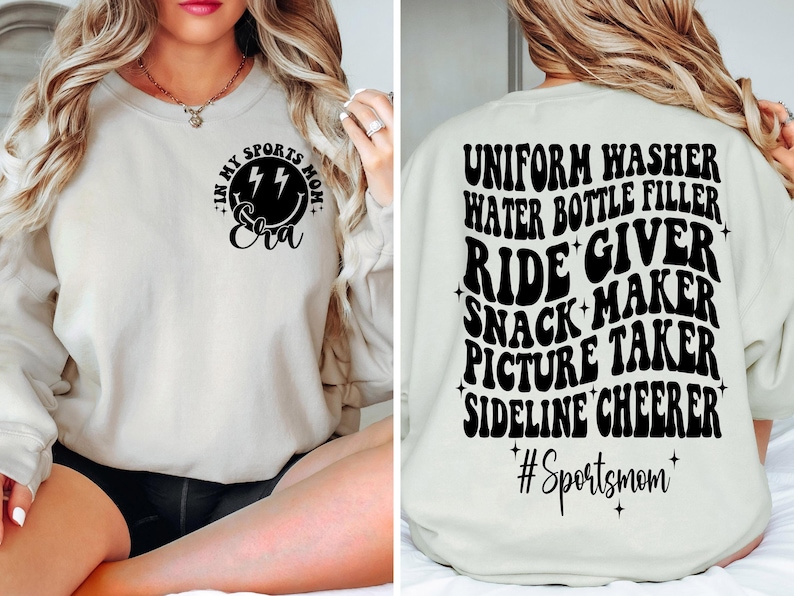 May include: A white sweatshirt with black text on the front and back. The front says "In My Sports Mom Eva" with a lightning bolt smiley face. The back says "Uniform Washer, Water Bottle Filler, Ride Giver, Snack Maker, Picture Taker, Sideline Cheerer #Sportsmom".