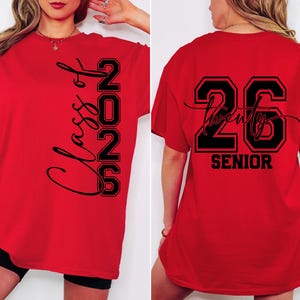 May include: Red t-shirt with black text. The front of the shirt says "Class of 2026" vertically. The back of the shirt says "26 Twenty Senior". The shirt is a graduation-themed item.
