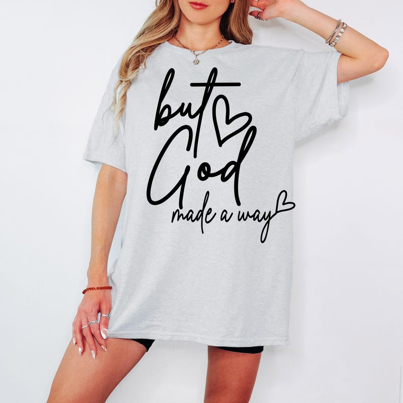 May include: A white t-shirt with black text that reads "but God made a way" with a heart symbol above the word "God" and another heart symbol at the end of the phrase.