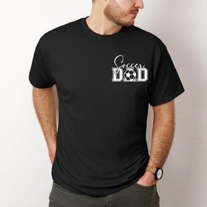 Peut inclure: T-shirt noir avec le texte blanc "Soccer Dad" et un ballon de football.