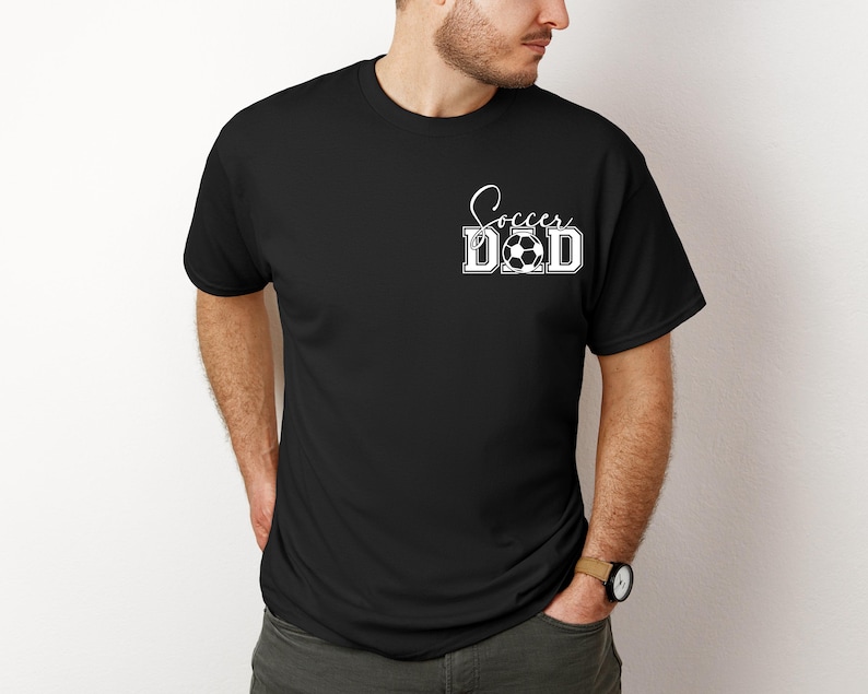 Peut inclure: T-shirt noir avec le texte blanc "Soccer Dad" et un ballon de football.