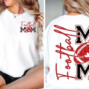 May include: White sweatshirt with "Football Mom" text and a football graphic in red and black. The back of the sweatshirt features the words "Football Mom" with a football graphic. The sweatshirt is a casual apparel item.
