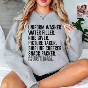May include: Gray sweatshirt with the text "UNIFORM WASHER. WATER FILLER. RIDE GIVER. PICTURE TAKER. SIDELINE CHEERER. SNACK PACKER. SPORTS MOM."