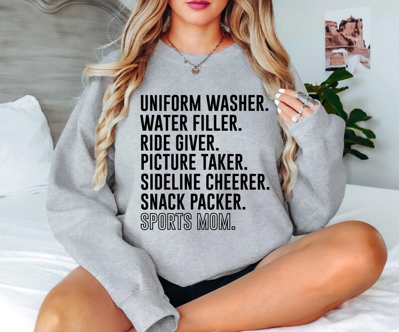 May include: Gray sweatshirt with the text "UNIFORM WASHER. WATER FILLER. RIDE GIVER. PICTURE TAKER. SIDELINE CHEERER. SNACK PACKER. SPORTS MOM."