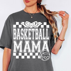 May include: Gray t-shirt with a white graphic design that says "Basketball Mama" with a checkered pattern and a basketball with a heart.