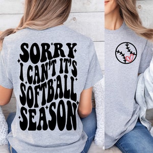 May include: A gray t-shirt with the text "Sorry I can't it's softball season" in black on the back. The front of the shirt has a black and red softball with a heart in the middle.