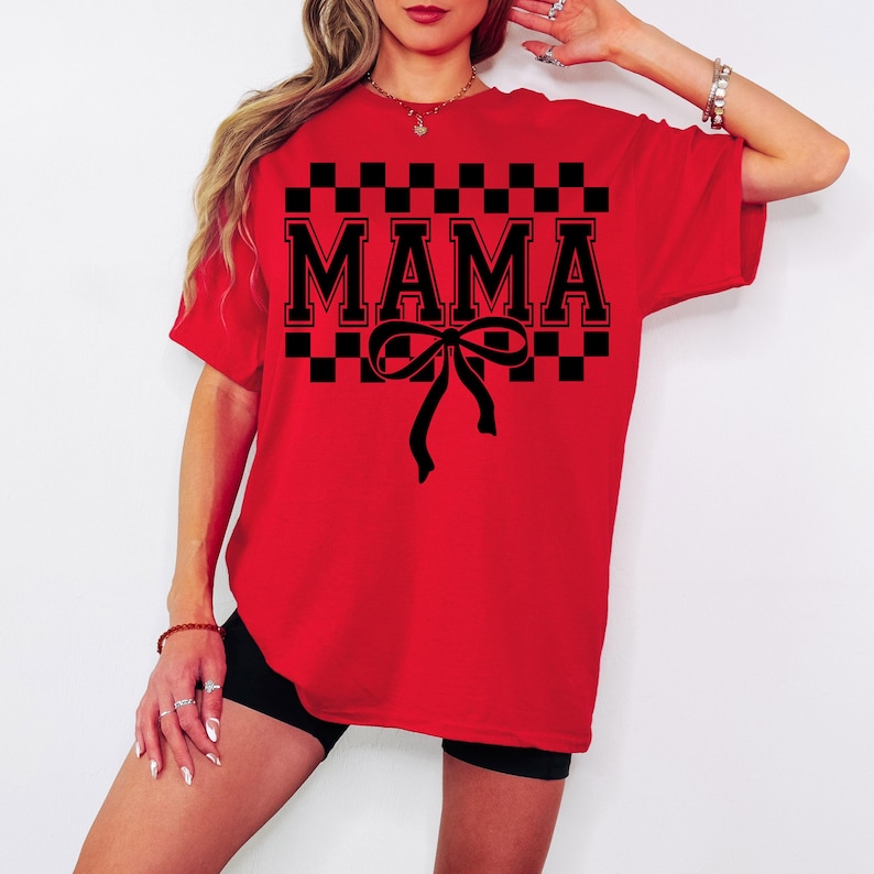 May include: Red t-shirt with a black checkered pattern and the word "MAMA" in black block letters. A black bow is centered below the word.