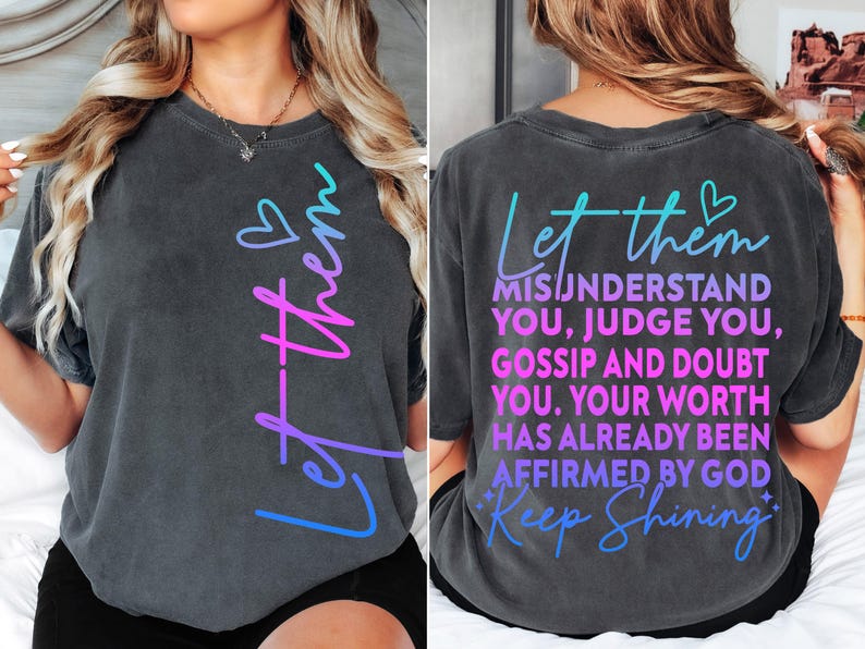 May include: Dark gray t-shirt with the words "Let them" in a gradient of blue and pink. The back of the shirt features the text "Misunderstand You, Judge You, Gossip and Doubt You. Your Worth Has Already Been Affirmed By God. Keep Shining."