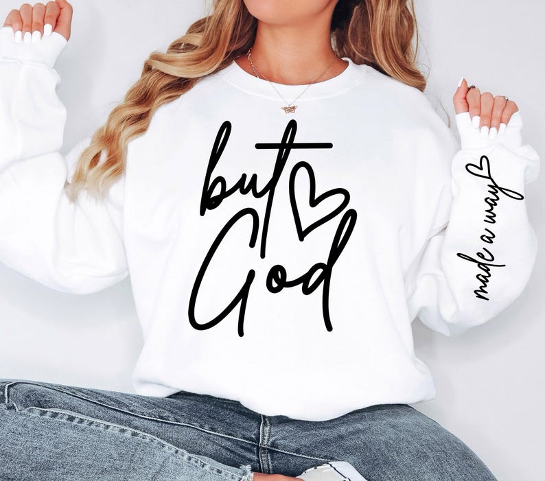 May include: White sweatshirt with the text "but God" in black script with a cross and heart. The right sleeve has the text "made a way" in black script.