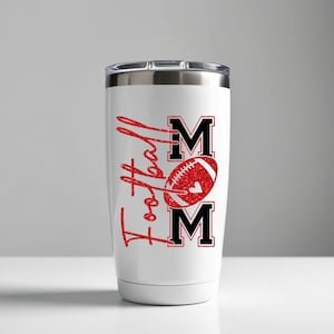 May include: White tumbler with a silver lid featuring the words "Football Mom" in red glitter script. The design includes a red football with a heart and the letters "MOM" in black.