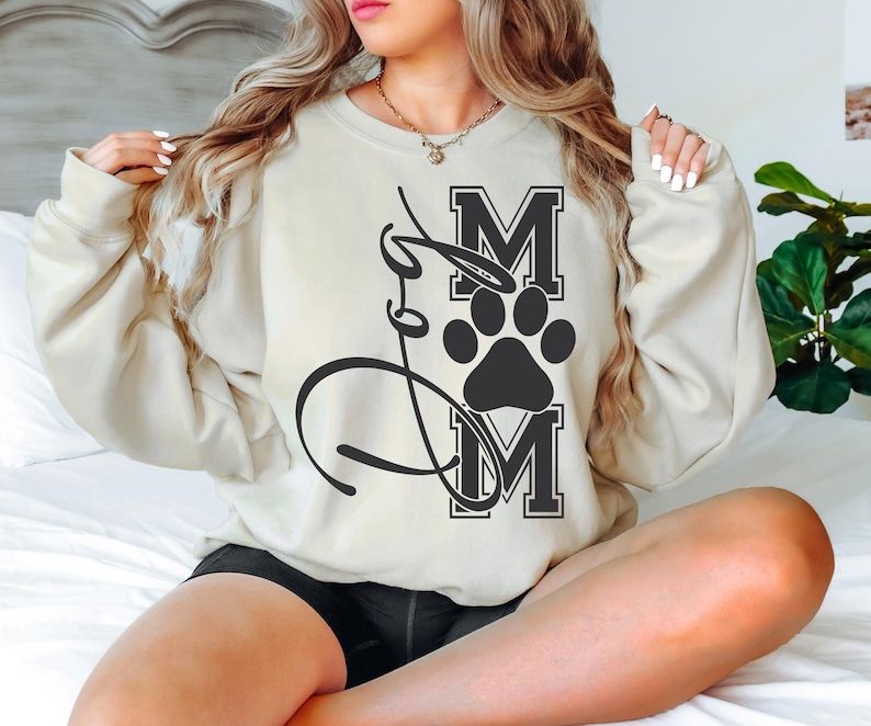 Puede incluir: Una sudadera de color crema con una huella de pata negra y el texto "Mom" en letras negras.