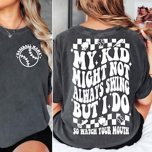 May include: A dark gray t-shirt with a white baseball graphic on the front and a white graphic on the back that says "My kid might not always swing but I do so watch your mouth".