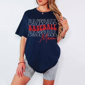 Pu&ograve; includere: Una maglietta blu navy con il testo "BASEBALL BASEBALL BASEBALL Mom" in lettere bianche e rosse glitter.