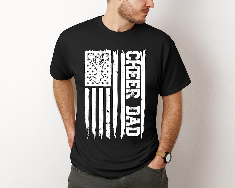 May include: Black t-shirt featuring a white distressed American flag design. The flag depicts a cheerleader silhouette and the text "Cheer Dad".