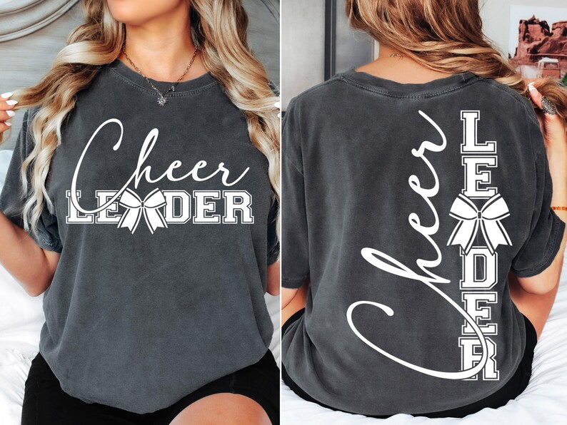 Puede incluir: Una camiseta gris oscuro con el texto "Cheer Leader" impreso en la parte delantera y el texto "Cheer Leader" impreso verticalmente en la parte posterior. El texto es blanco e incluye un lazo blanco.