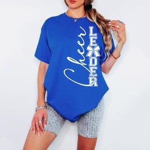 Puede incluir: Una camiseta azul real con texto blanco que dice "Cheer Leader" con un lazo blanco en el medio de la palabra "Leader".