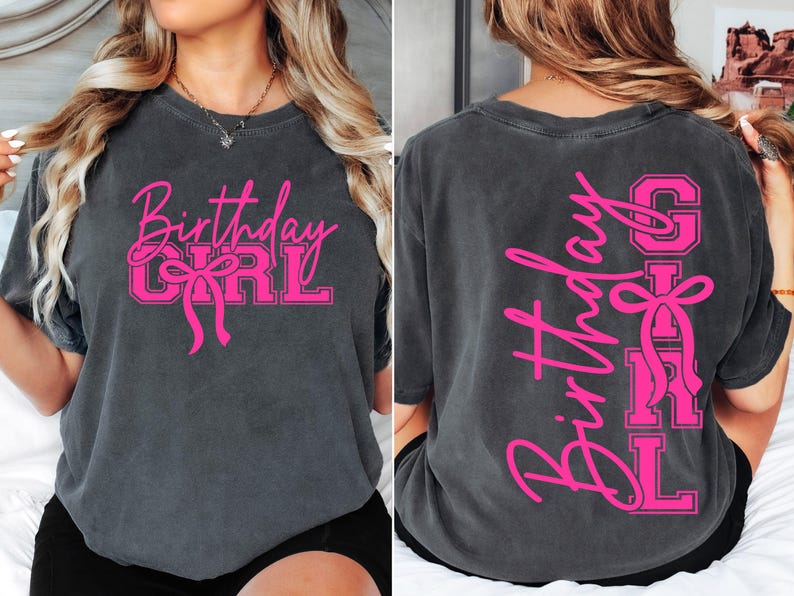 May include: Charcoal grey t-shirt with the words "Birthday Girl" in pink script and block letters, featuring a bow graphic. The same design is on the back, vertically. A casual, comfortable tee for a birthday celebration.