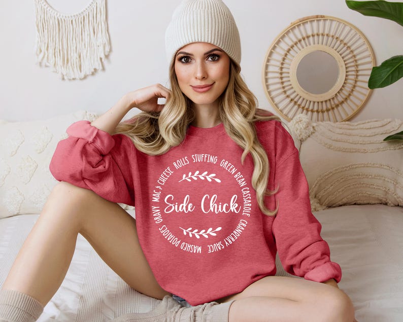 May include: A red sweatshirt with a white circle graphic that says "Side Chick" and lists various Thanksgiving foods around the circle. The model is wearing a white beanie.