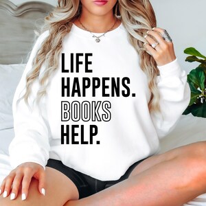 May include: White sweatshirt with black text that reads "Life Happens. Books Help."