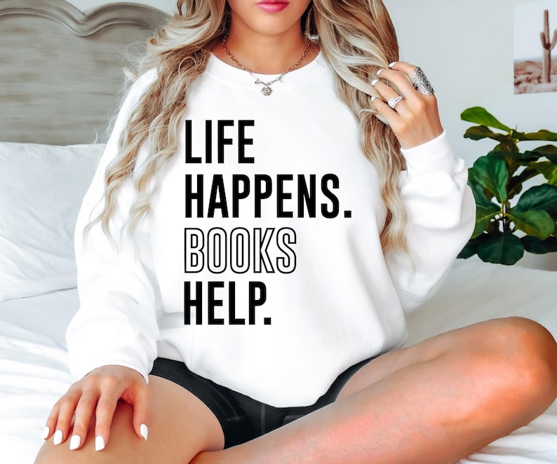 May include: White sweatshirt with black text that reads "Life Happens. Books Help."