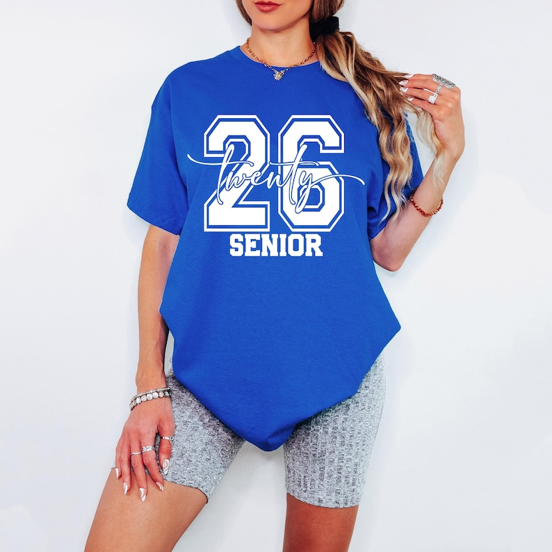 May include: Royal blue t-shirt with the number "26" and the word "twenty" in a script font, and the word "SENIOR" in a block font. The shirt is a short-sleeved, crew neck style.