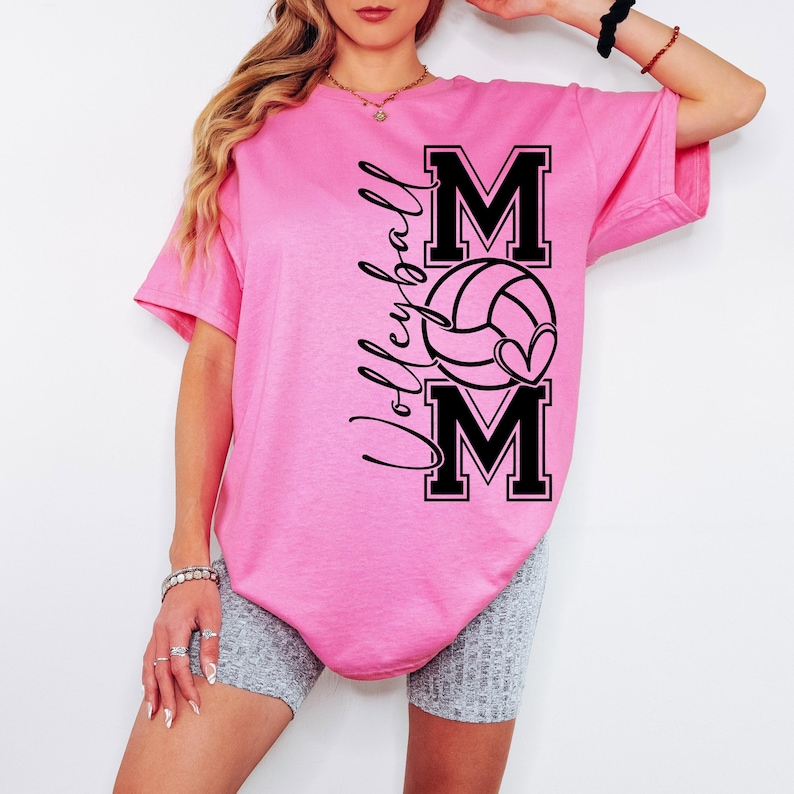 May include: Pink t-shirt with a black graphic design that says "Volleyball Mom" with a volleyball and heart.