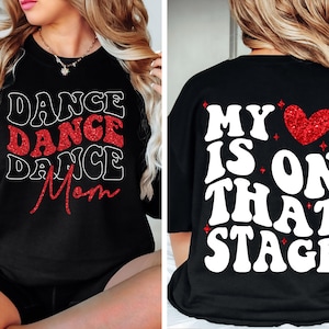 May include: Black sweatshirt with the words "DANCE DANCE DANCE Mom" in white and red glitter lettering on the front. The back of the shirt says "MY HEART IS ON THAT STAGE" in white lettering with a red glitter heart.