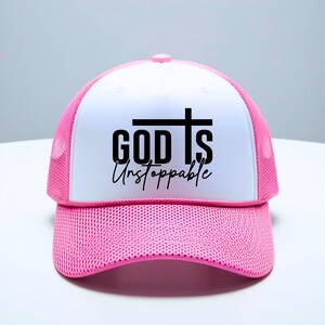 May include: A pink and white trucker hat with the words "GOD IS Unstoppable" in black script and a cross design. The hat features a mesh back and a curved brim, suitable for casual wear.
