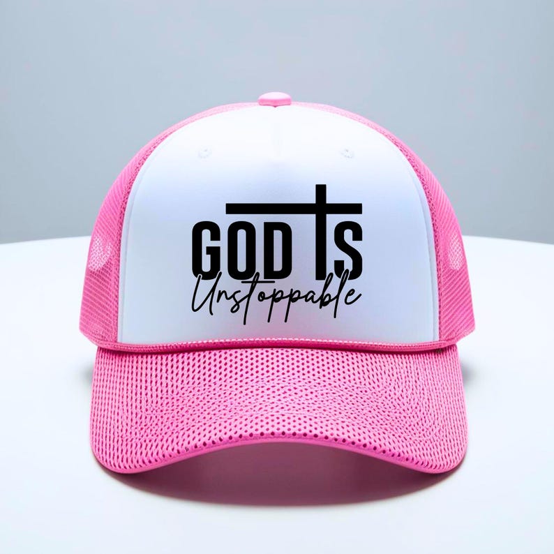 May include: A pink and white trucker hat with the words "GOD IS Unstoppable" in black script and a cross design. The hat features a mesh back and a curved brim, suitable for casual wear.