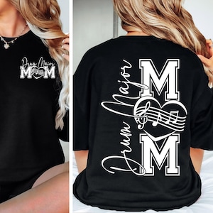 May include: Black sweatshirt with white text that reads "Drum Major Mom" with a musical note heart design. The front of the shirt has the same design. A stylish and comfortable top for music lovers.