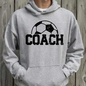 May include: A gray hooded sweatshirt with a black soccer ball graphic and the word "COACH" printed in black.