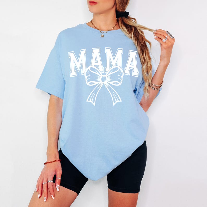 May include: A light blue t-shirt with the word "MAMA" in white block letters and a white bow underneath.