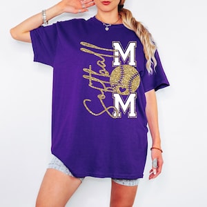 May include: A purple t-shirt with a gold glitter design. The design features the word "MOM" with a baseball in the center. The baseball is gold glitter, and the letters "M" are white.