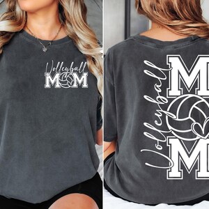 May include: A dark gray t-shirt with the text "Volleyball Mom" and a volleyball graphic on the front. The back of the shirt has the text "Volleyball Mom" with a volleyball and heart graphic.