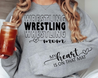 以下が含まれることがあります： 「Wrestling Wrestling Wrestling Mom」と「My heart is on that mat」というテキストとハートマークが書かれたグレーのスウェットシャツです。