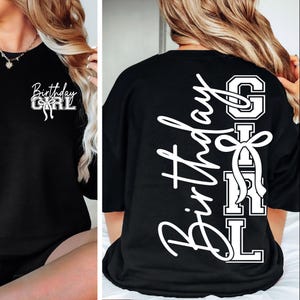 May include: Black t-shirt featuring the text "Birthday Girl" in white script and block letters. The front of the shirt displays "Birthday Girl" with a bow. The back has "Birthday Girl" written vertically.