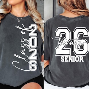 May include: Dark gray t-shirt with white text. The front reads "Class of 2026" vertically. The back displays "26 Twenty Senior" in a collegiate style. A comfortable, casual tee for graduation.