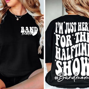 Puede incluir: Camiseta negra con texto blanco que dice "I'm just here for the halftime show #Bandmom" en la parte posterior y "Band mom" con un coraz&oacute;n en la parte delantera.