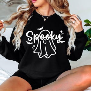 Op de afbeelding: Zwart sweatshirt met een witte afbeelding van een spook en het woord "Spooky" met vleermuizen en sterren.