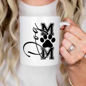 Puede incluir: Taza de caf&eacute; de cer&aacute;mica blanca con una huella de pata negra y el texto "Mom" en una fuente negra en bloque.