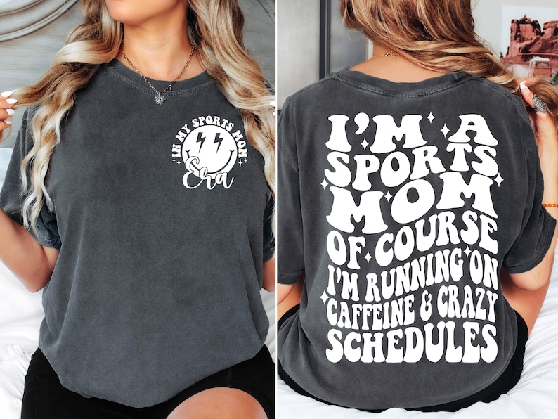 Pode incluir: Uma camiseta cinza escura com um gr&aacute;fico branco na frente que diz "In My Sports Mom Era" com um rosto sorridente e raios. A parte de tr&aacute;s da camiseta tem um gr&aacute;fico branco que diz "I'm a Sports Mom of Course I'm Running on Caffeine & Crazy Schedules".